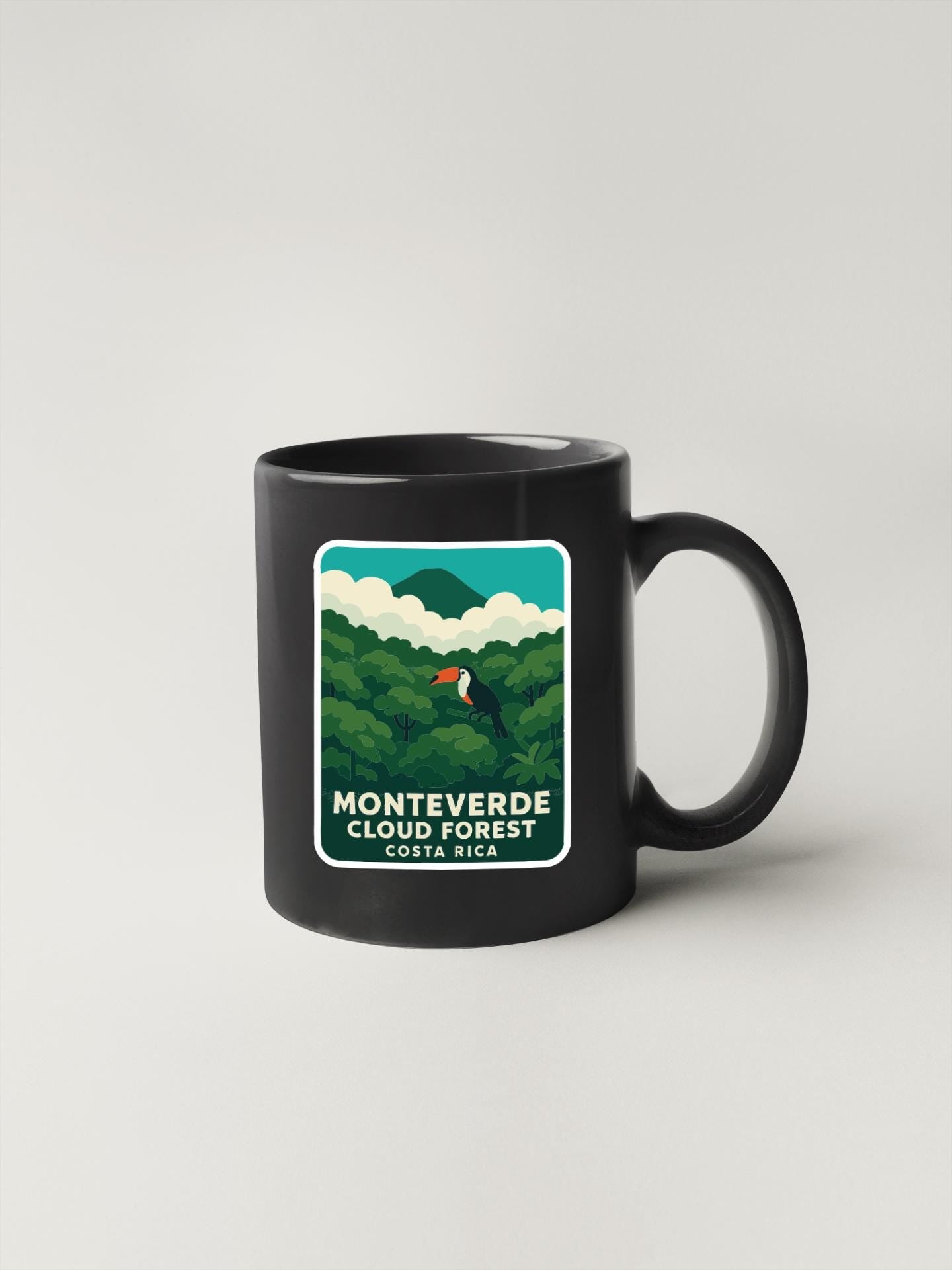 A black coffee mug with a graphic design depicting a tropical forest scene, including a toucan and lush vegetation.