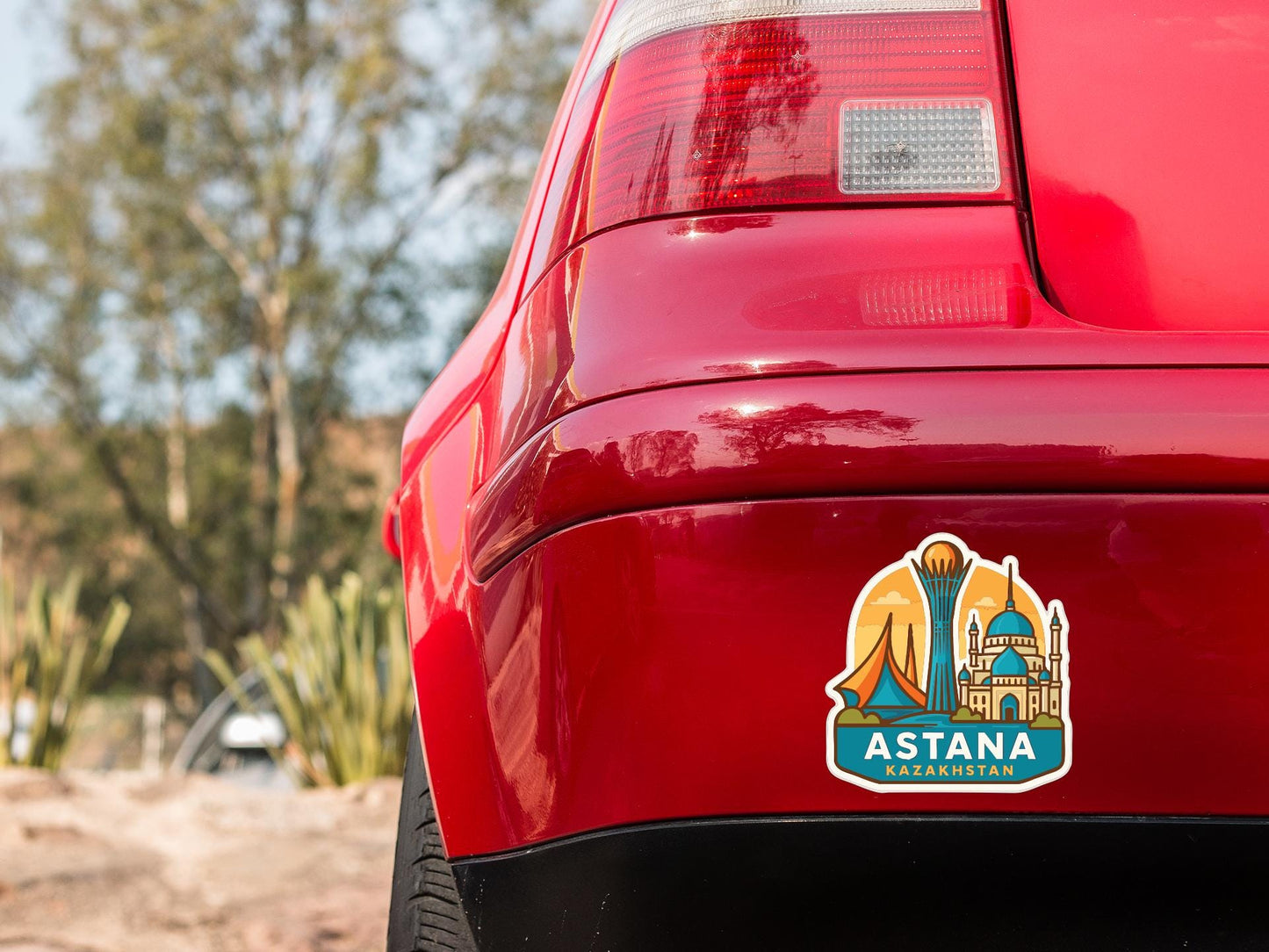 the rear end of a red car with a sticker on the trunk that features an illustration of a city skyline.