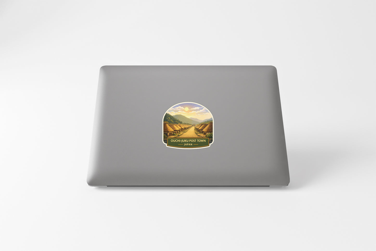 A sticker on the back of a laptop, depicting a scenic landscape with mountains and a winding road.