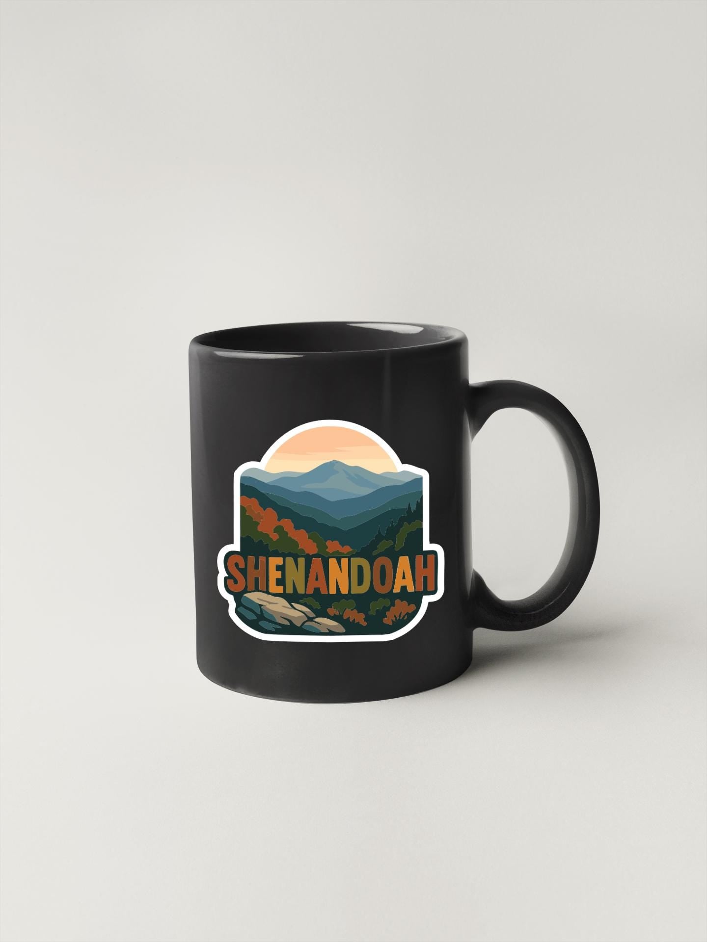 A black coffee mug with a sticker depicting a scenic mountain landscape and the text "SHENANDOAH" printed on it.