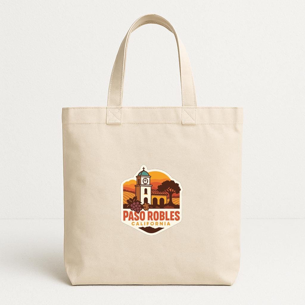 A beige tote bag with a graphic design featuring a clock tower and the text "PASO ROBLES CALIFORNIA".