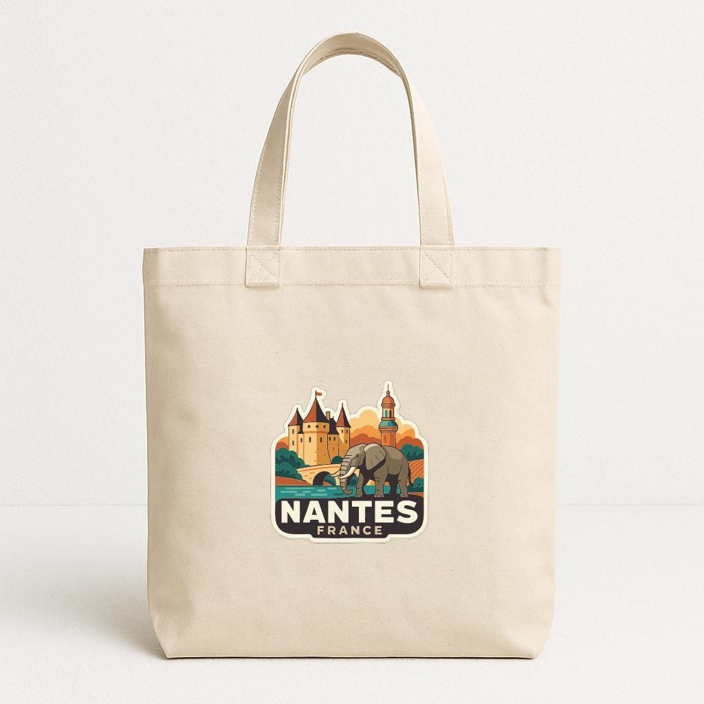 A beige tote bag with a printed design featuring a castle and an elephant, along with the text "NANTES FRANCE".