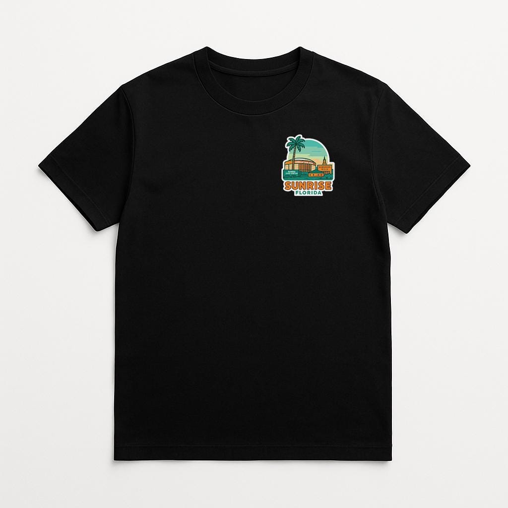 A black t-shirt with a graphic design on the front, depicting a tropical scene with palm trees and a building.