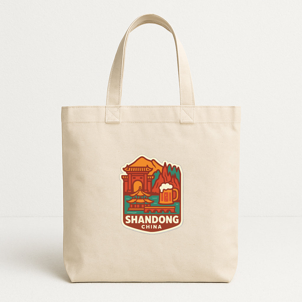 A beige tote bag with a printed design depicting Shandong, China, including a temple, mountains, and a beer mug.