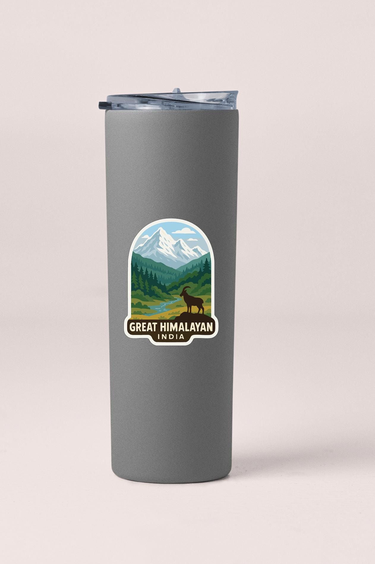A gray tumbler with a sticker depicting a mountain landscape and a mountain goat.