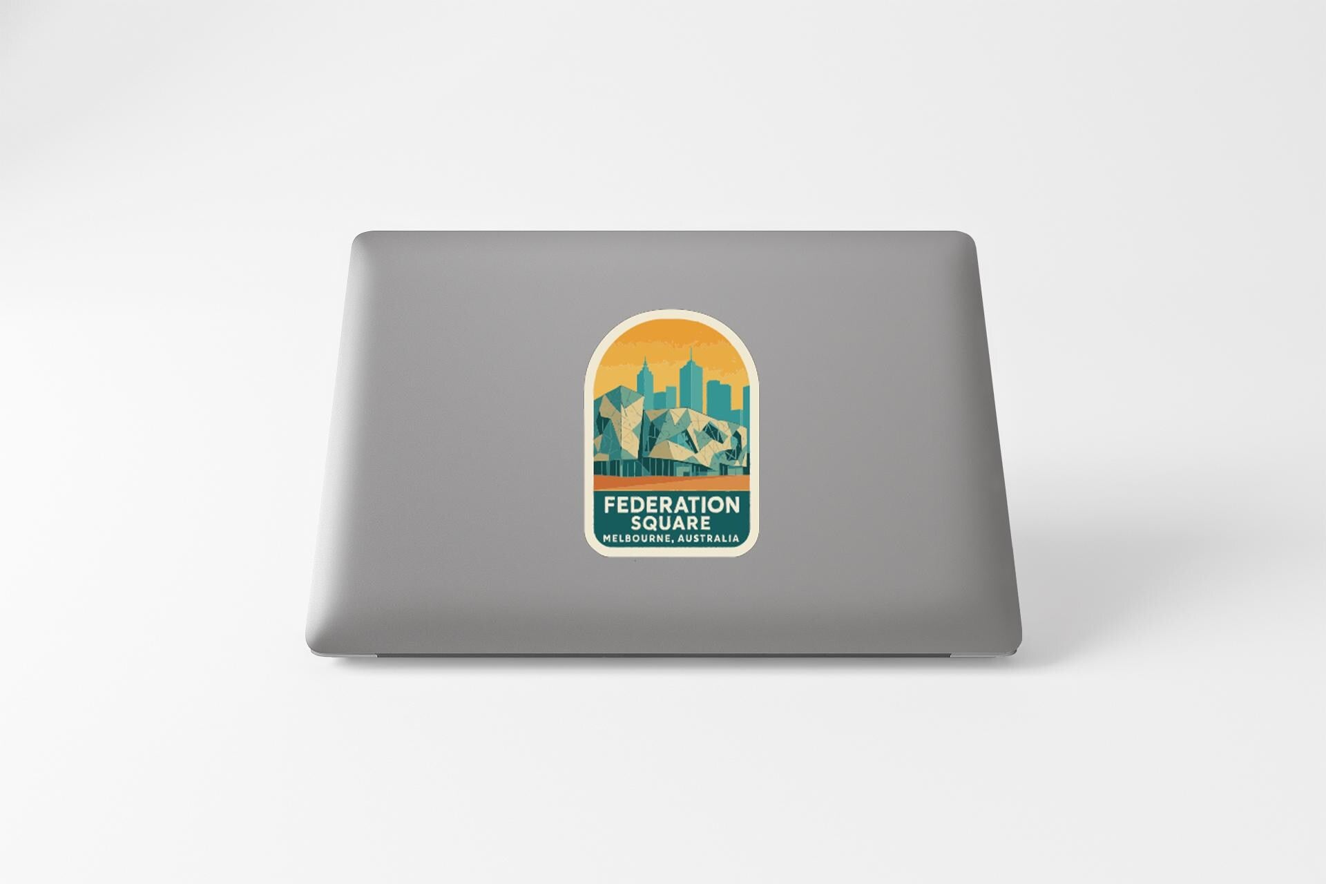 a sticker with a graphic of a cityscape and the text "FEDERATION SQUARE MELBOURNE AUSTRALIA" on a grey laptop.