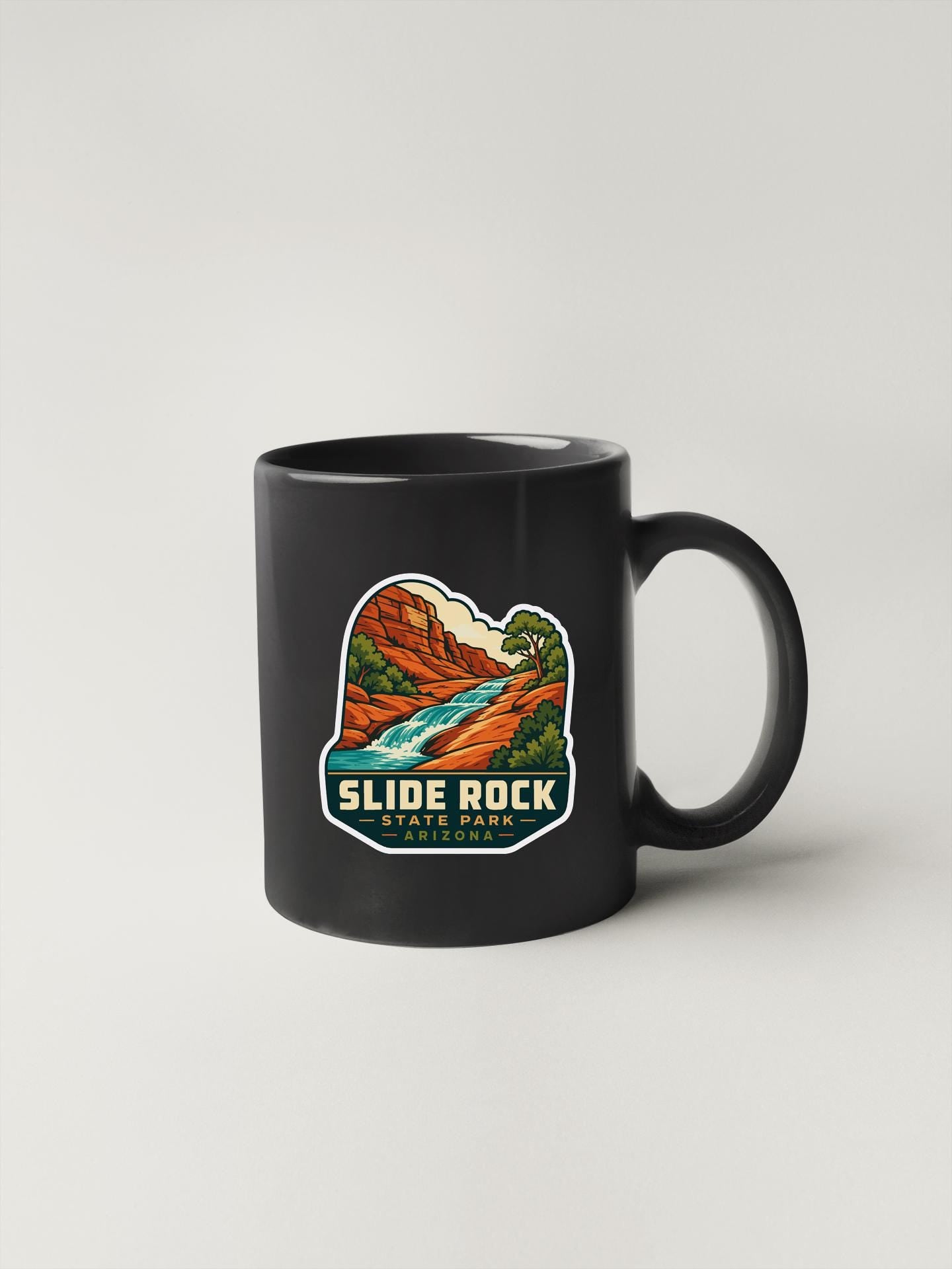 A black coffee mug with a colorful graphic depicting a scenic landscape, including a river and mountains, along with the text "SLIDE ROCK STATE PARK ARIZONA".