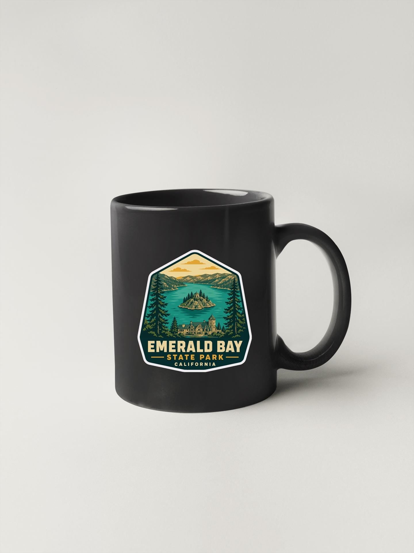 A black coffee mug with a graphic design depicting a scenic landscape featuring a lake, mountains, and pine trees.