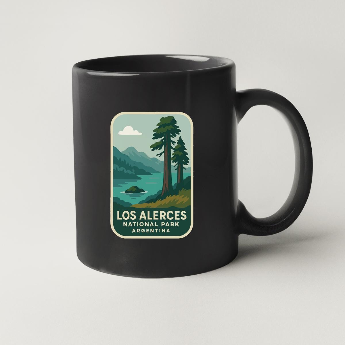A black coffee mug with a graphic design depicting a scenic landscape with mountains, trees, and a lake.