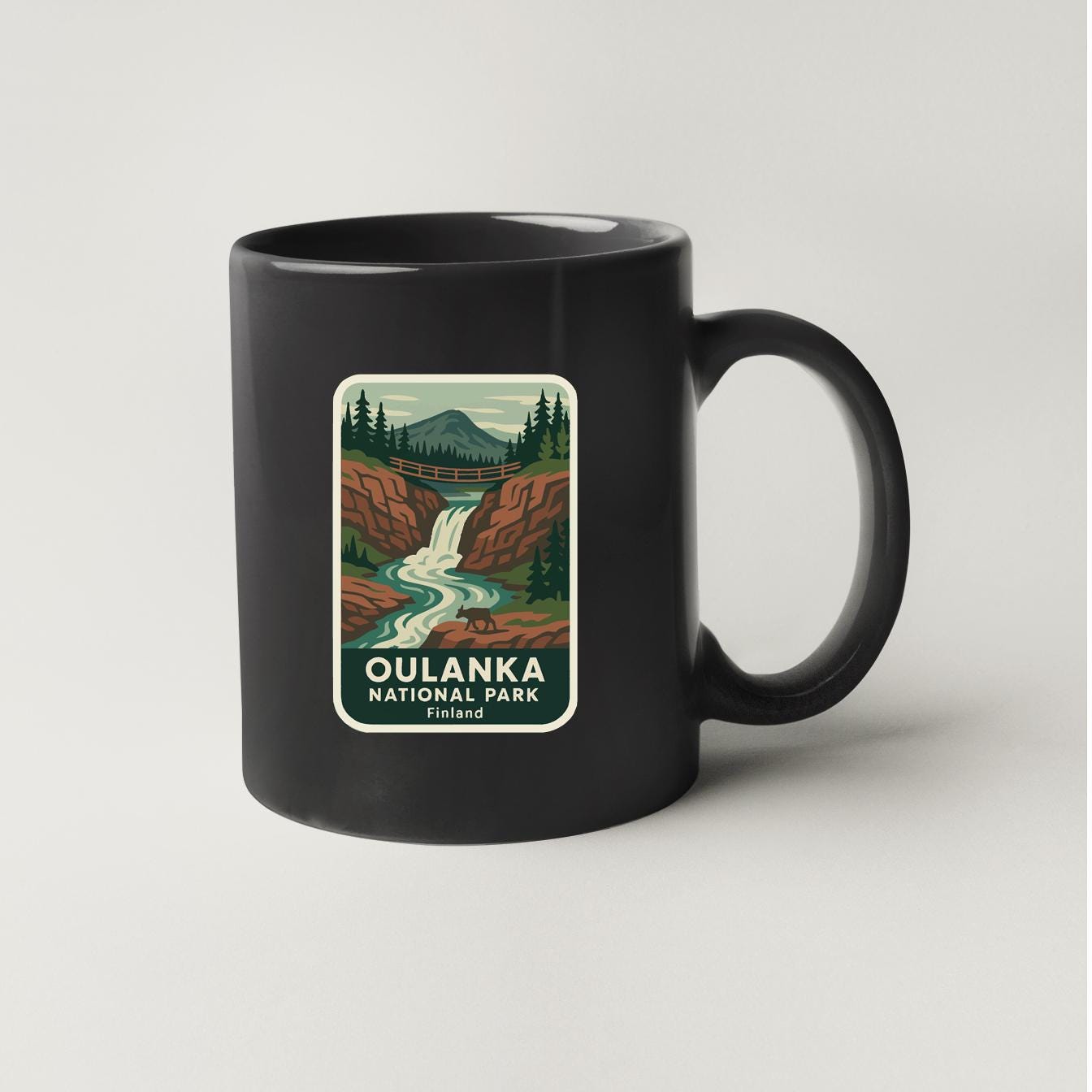 A black coffee mug with a label that features a scenic illustration of Oulanka National Park in Finland.