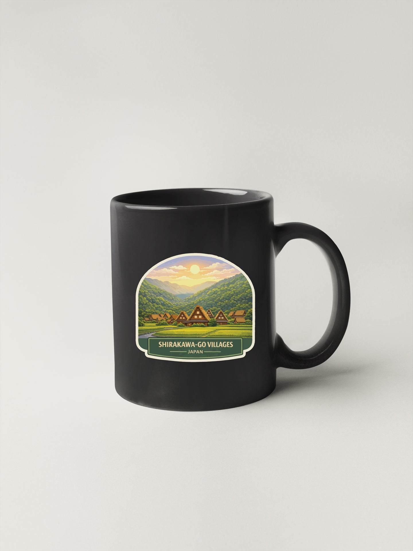 A black coffee mug with a label depicting a scenic landscape with a village and mountains in the background.