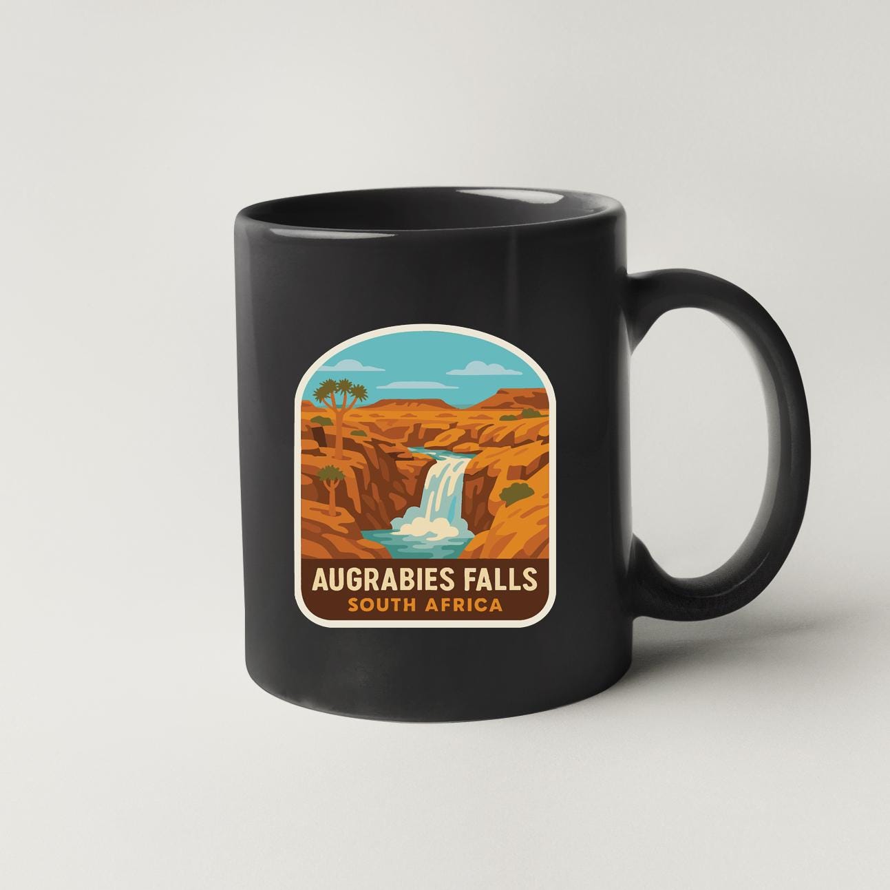 A black coffee mug with a graphic design depicting a waterfall and a desert landscape.