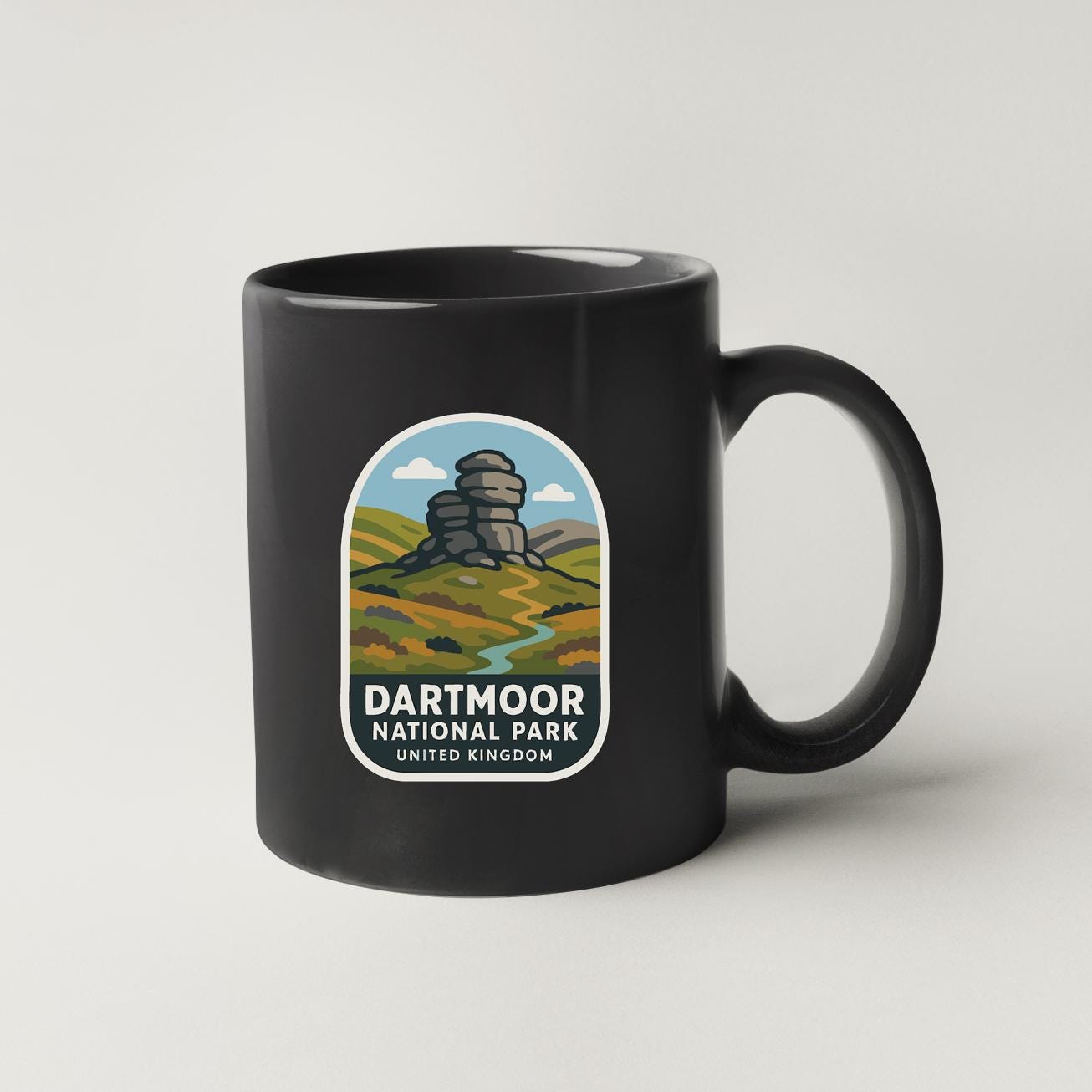A black coffee mug with a graphic design depicting a scenic landscape with a rock formation and a river.