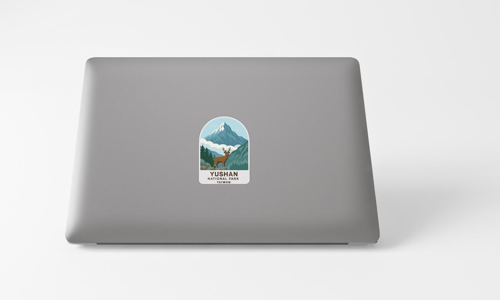 A sticker on the back of a laptop, depicting a mountain landscape with a deer.