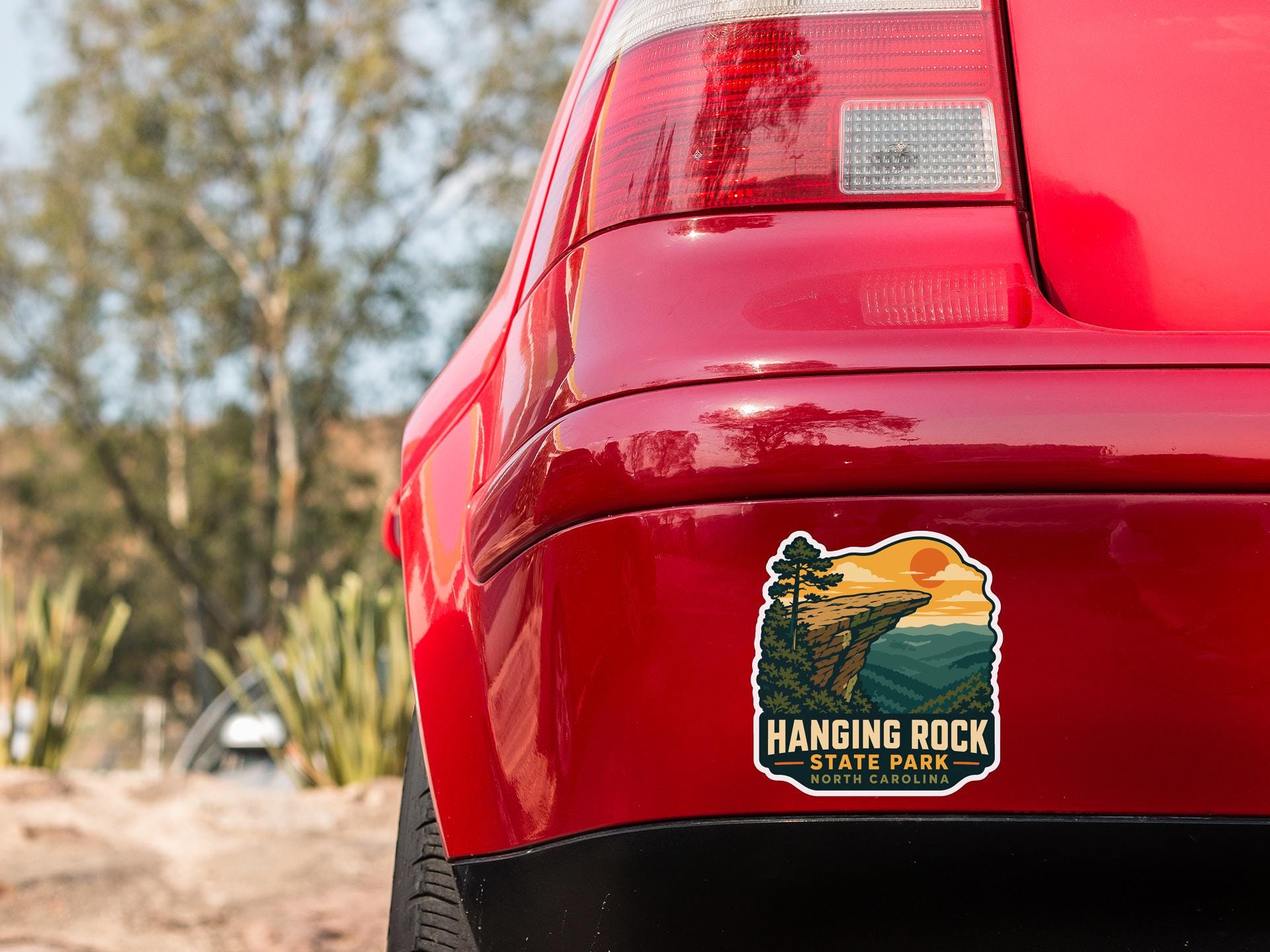 the rear end of a red car with a sticker on the trunk that says "Hanging Rock State Park North Carolina".