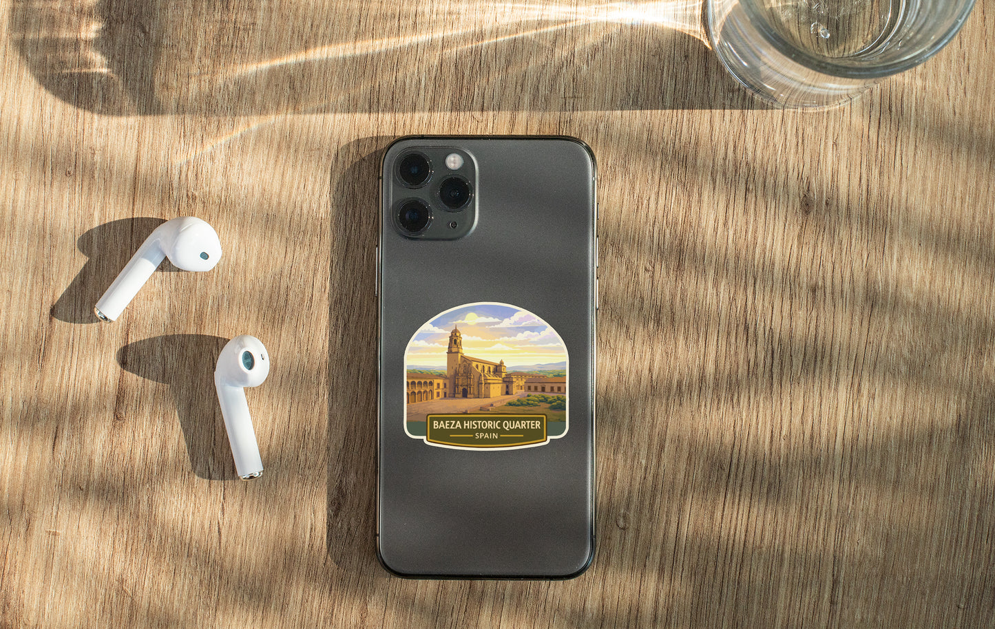 a smartphone with a sticker of a building, a pair of white earbuds, and a glass of water on a wooden surface.