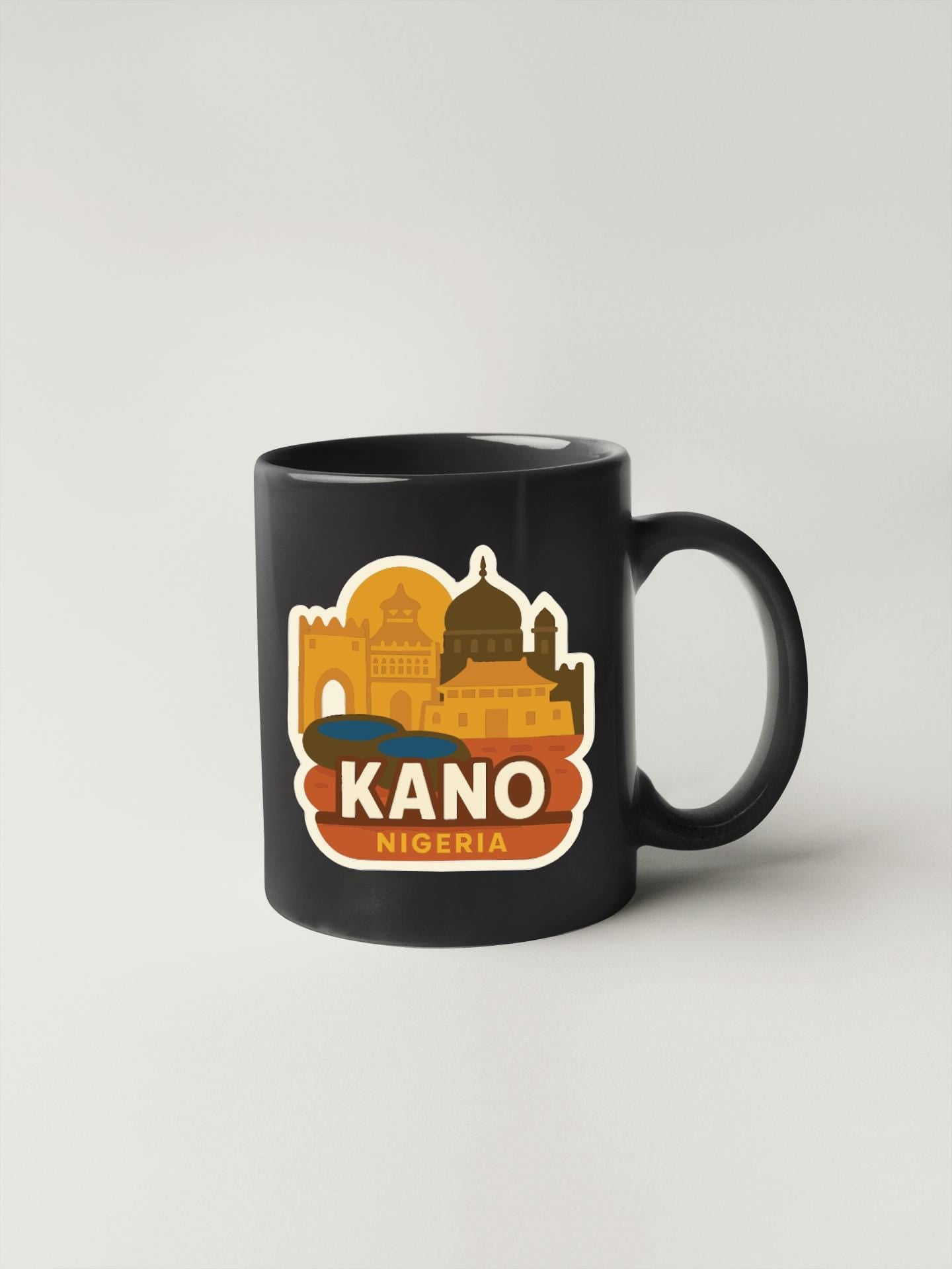 A black coffee mug with a colorful sticker depicting the skyline of Kano, Nigeria.