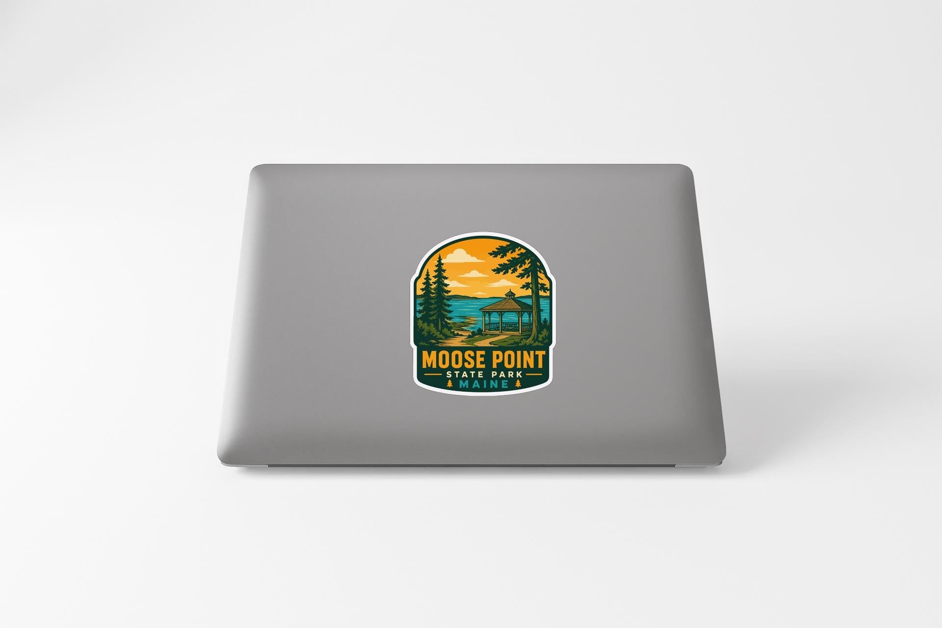 A sticker on the back of a laptop that features a scenic landscape with a lake, mountains, and pine trees, along with the text "MOOSE POINT STATE PARK".