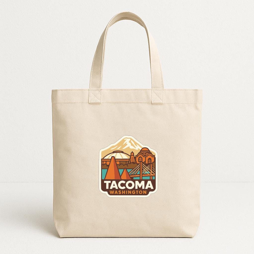 A beige tote bag with a printed design featuring a mountain and a city skyline, along with the text "TACOMA WASHINGTON".