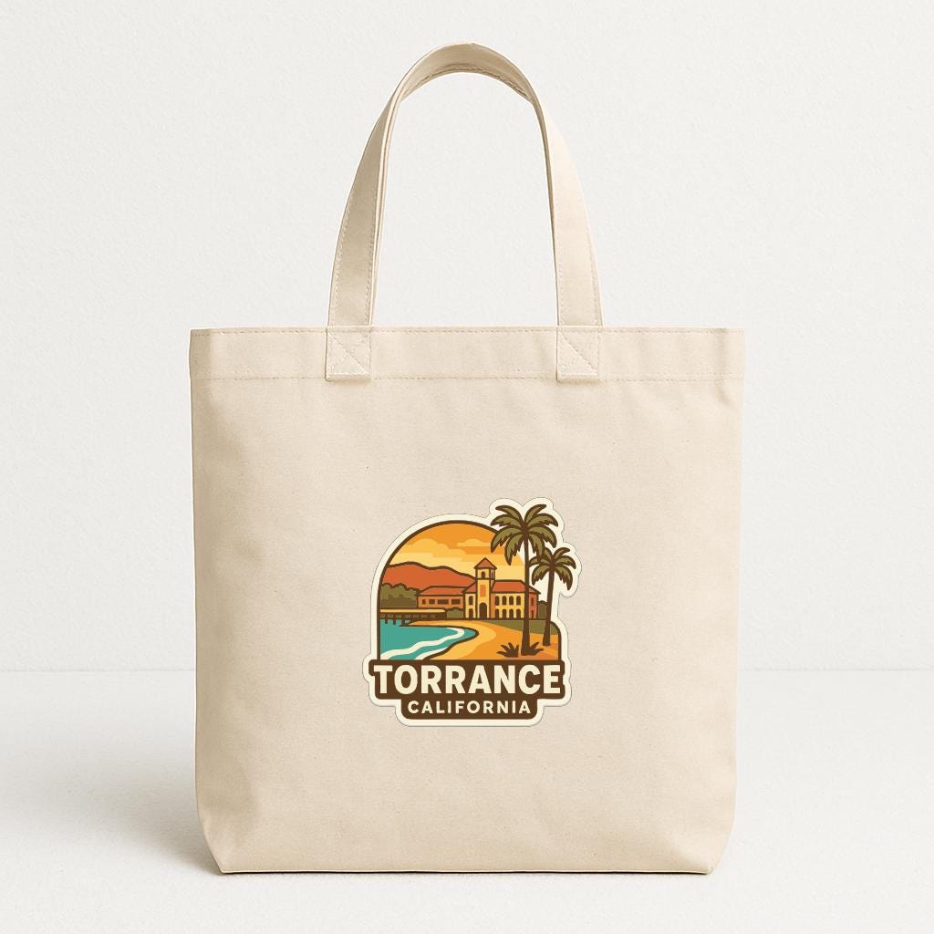 A beige tote bag with a printed design depicting a beach scene and a palm tree, along with the text "TORRANCE CALIFORNIA".