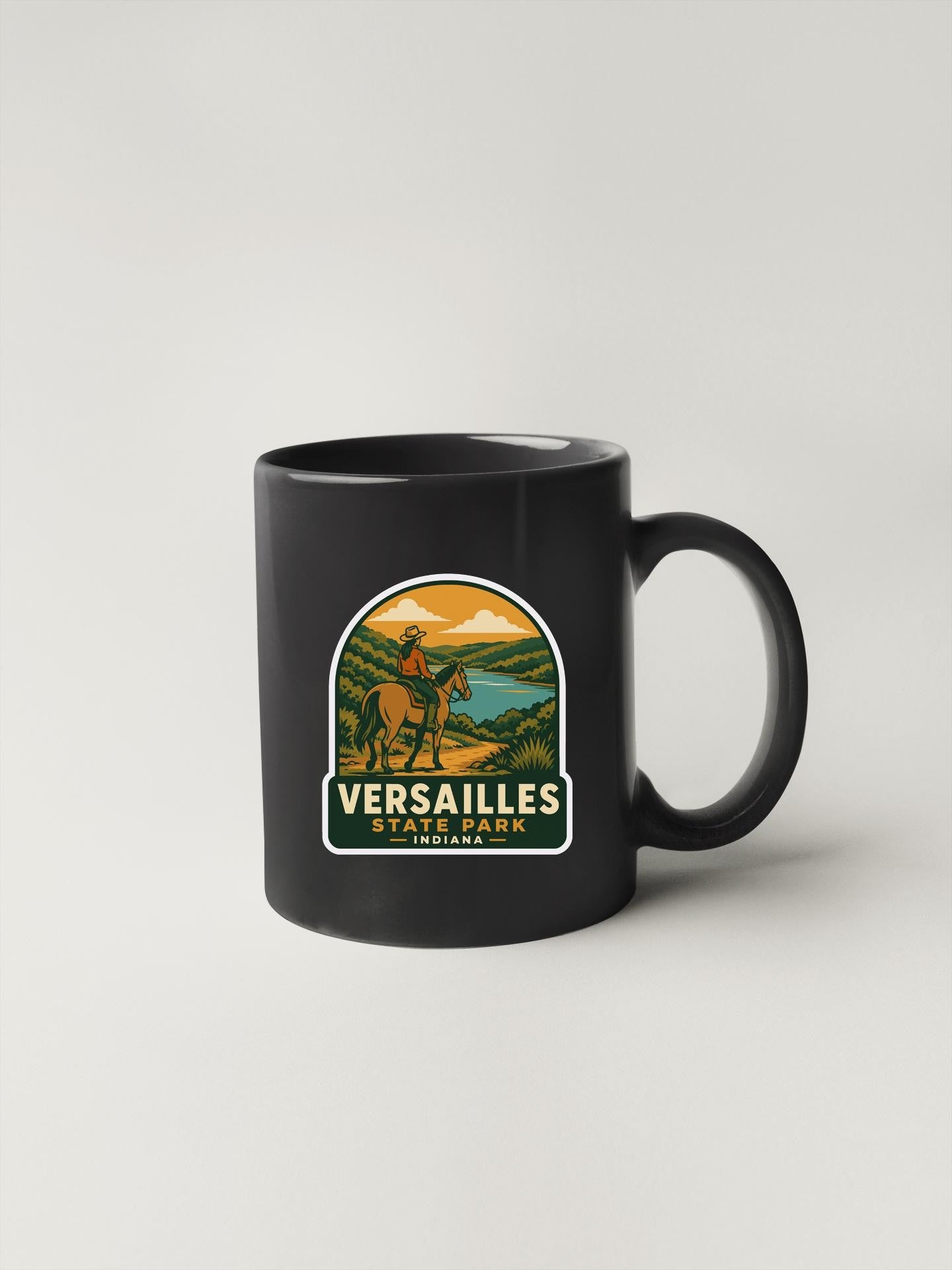A black coffee mug with a graphic design depicting a person riding a horse in a scenic landscape.
