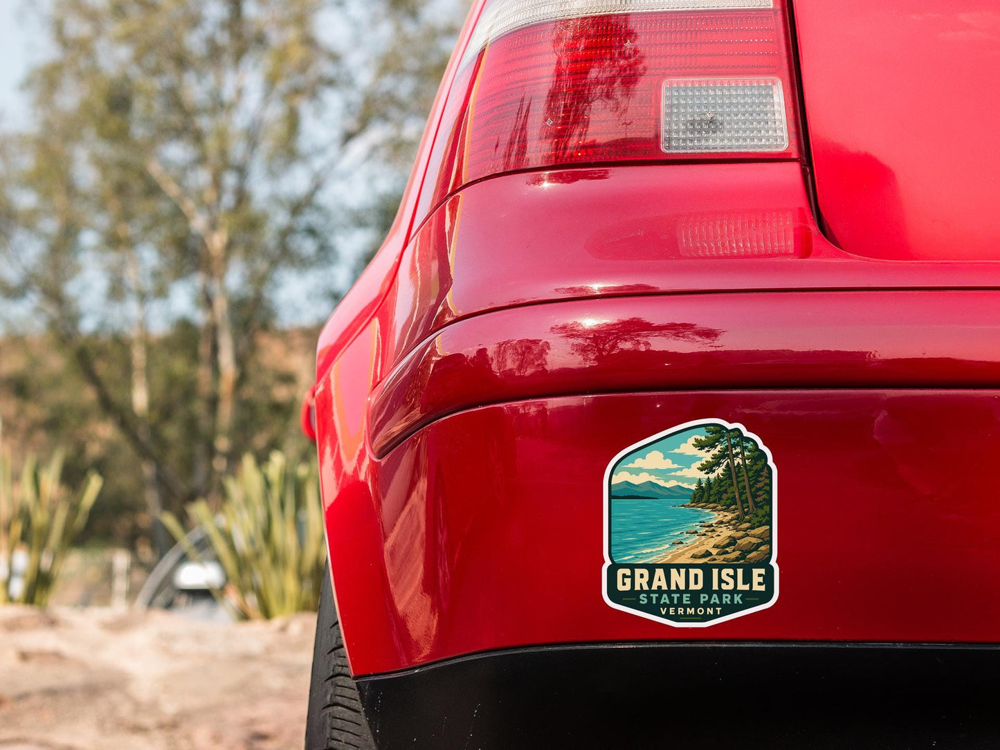 the rear end of a red car with a sticker on the trunk that says "Grand Isle State Park, Vermonters".