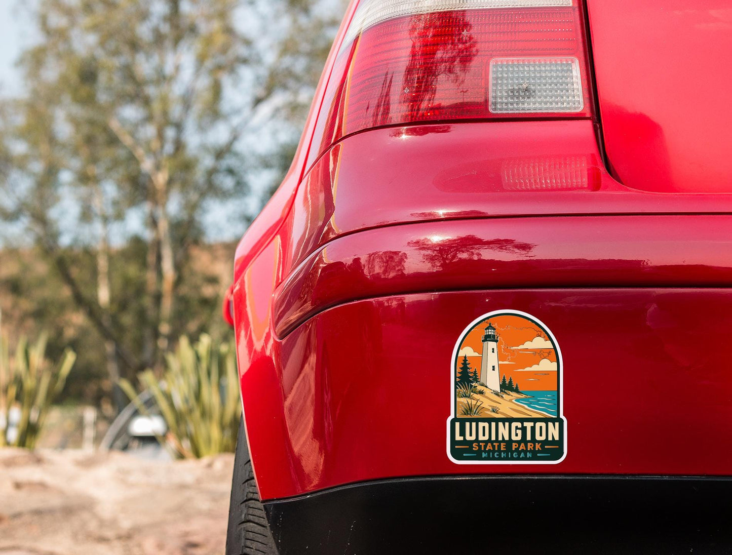 the rear end of a red car with a sticker on the trunk that says "Ludington State Park, Michigan".