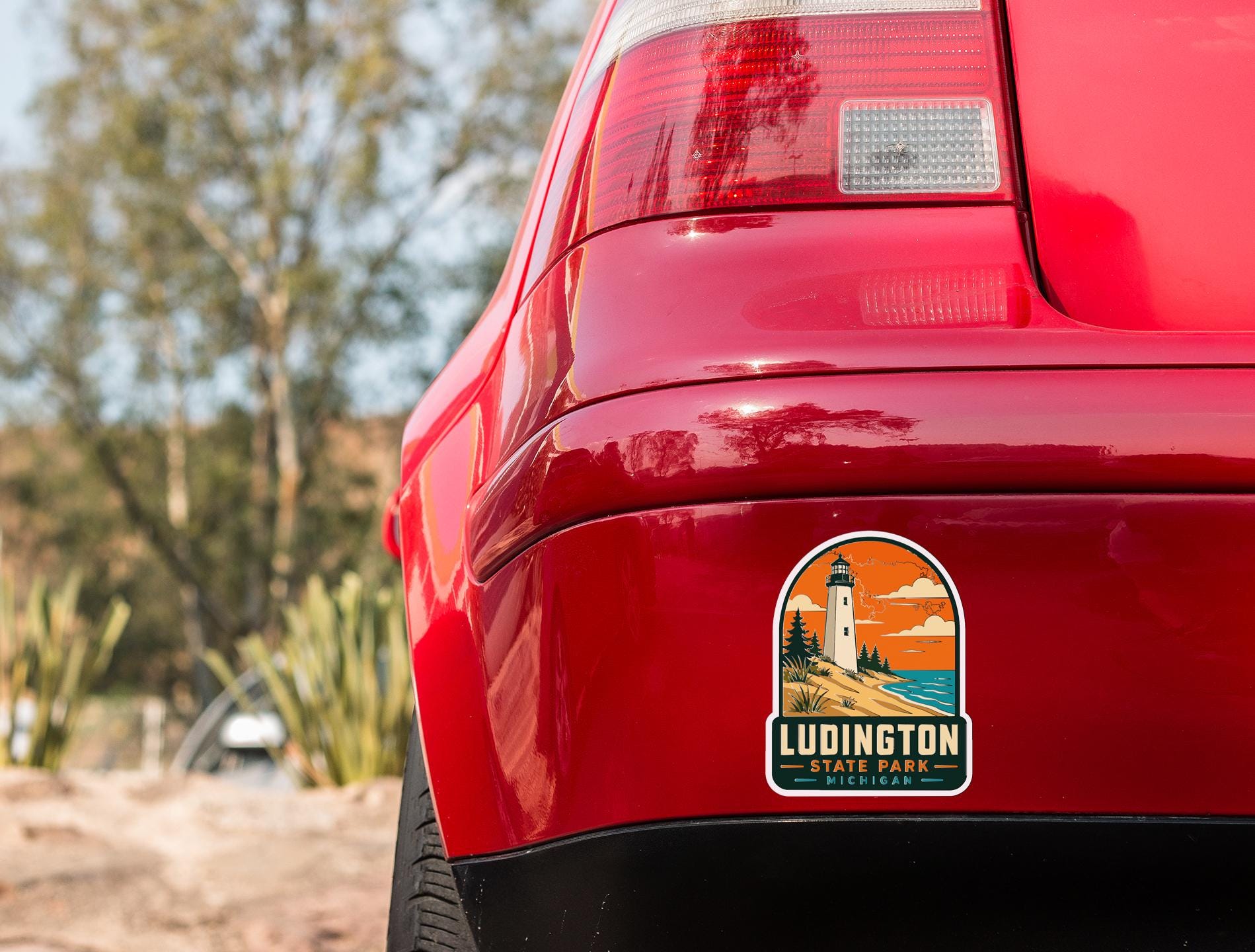 the rear end of a red car with a sticker on the trunk that says "Ludington State Park, Michigan".