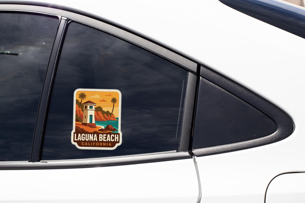 A sticker on the side of a car window, depicting a scenic beach with a lighthouse and palm trees, advertising Laguna Beach, California.