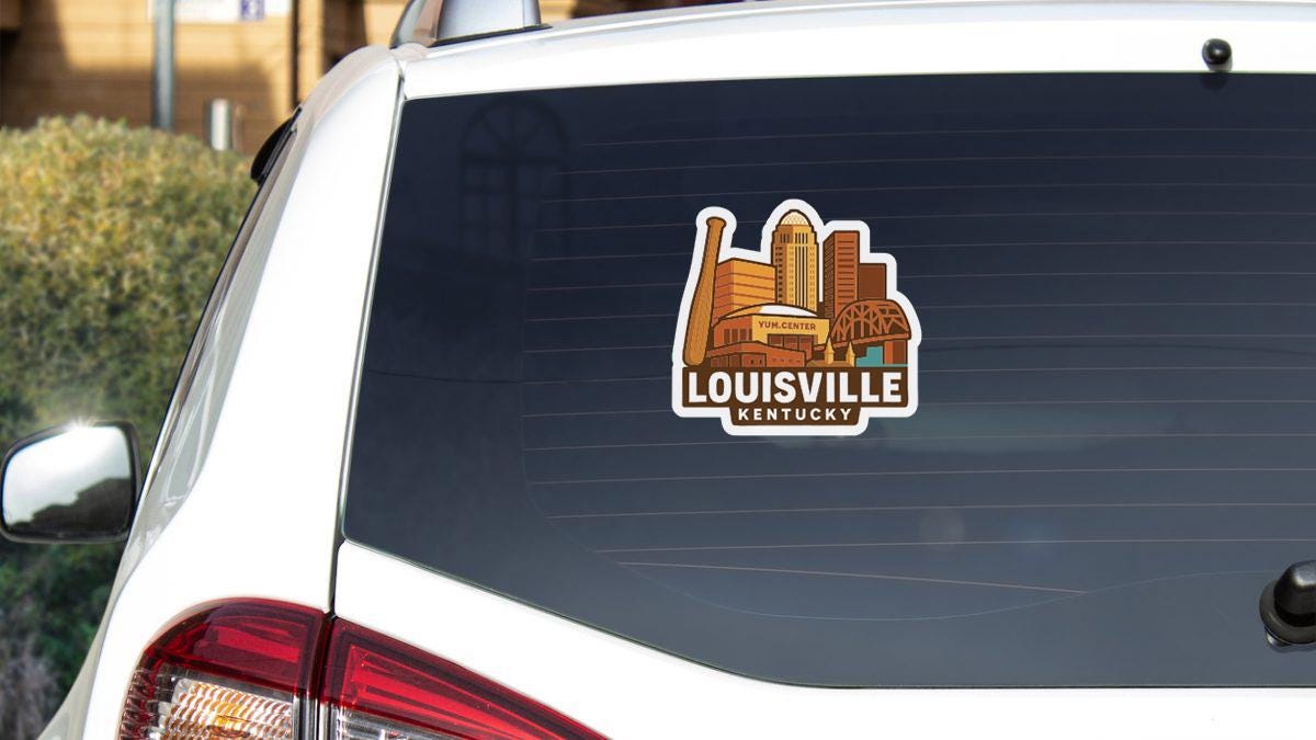 A sticker on the rear window of a white vehicle, depicting the skyline of Louisville, Kentucky.