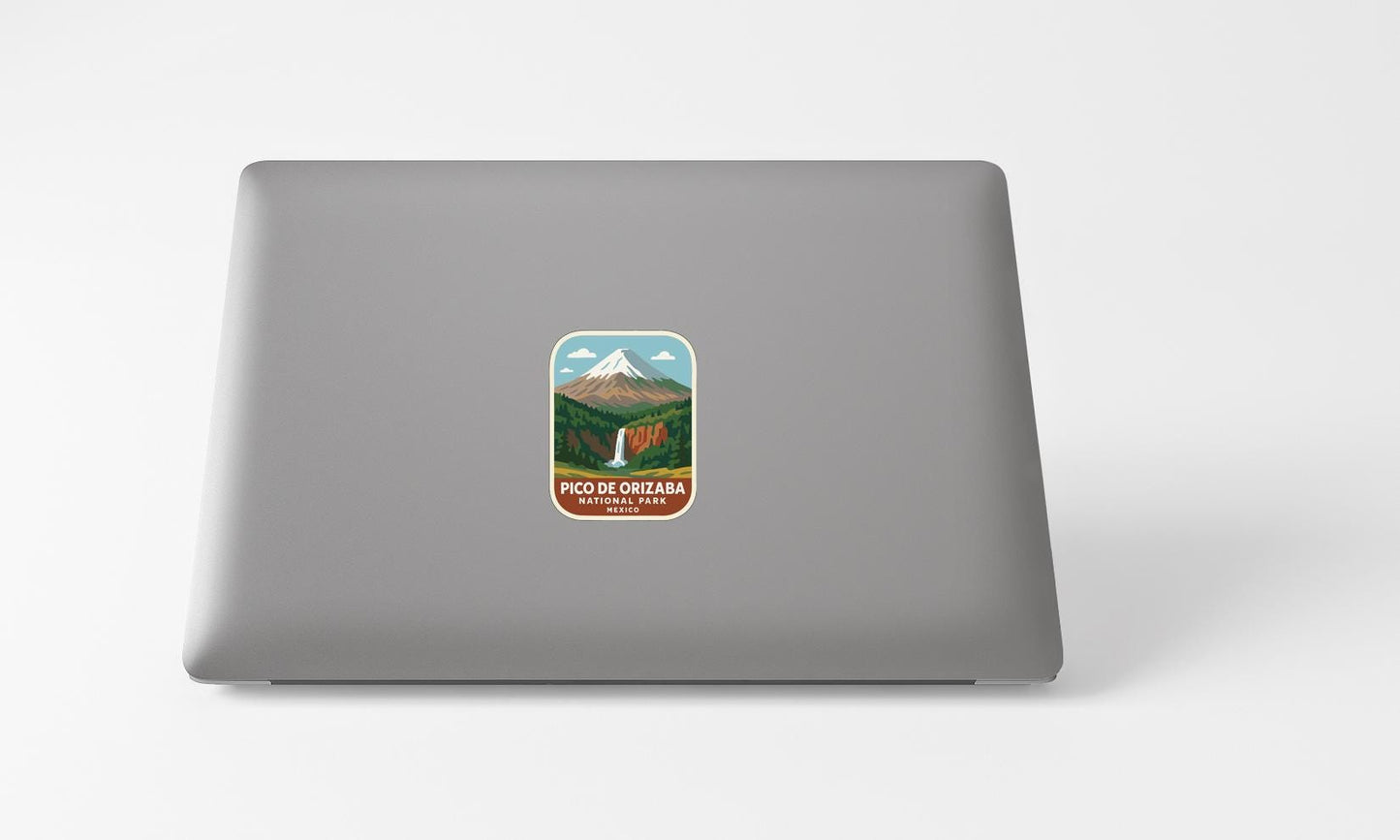 A sticker with a mountain landscape and a waterfall is placed on the back of a laptop computer.