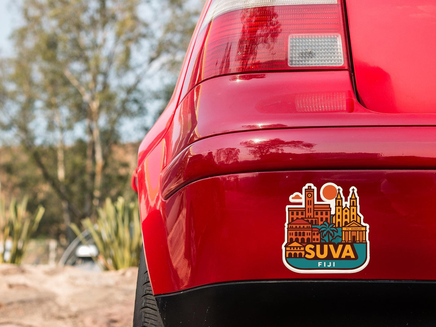 the rear end of a red car with a sticker on the trunk that features a cityscape of Fiji.