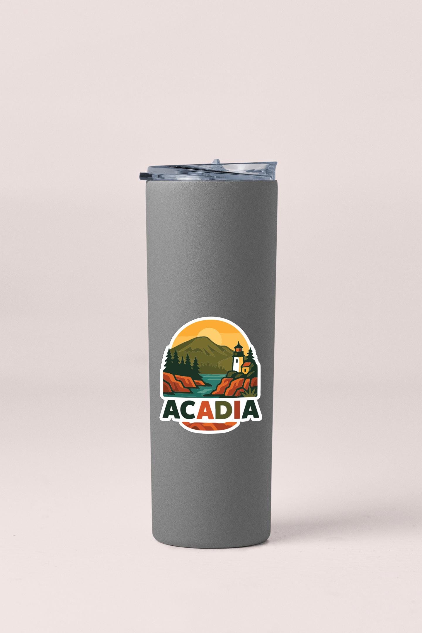 A gray insulated tumbler with a lid and a circular logo featuring a mountain landscape and a lighthouse.