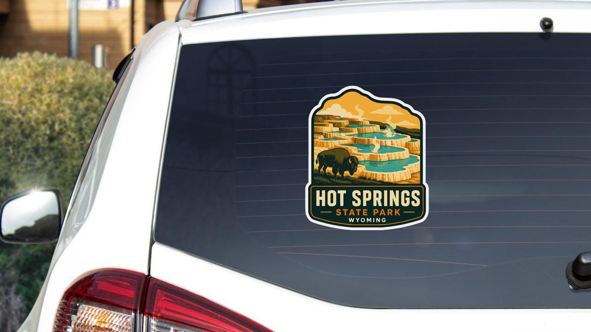 A sticker on the rear window of a white car, depicting a scenic landscape with a large body of water and a bison in the foreground.
