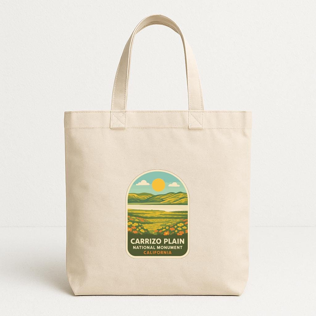 A beige tote bag with a graphic design depicting a scenic landscape, including mountains, a river, and a sun.