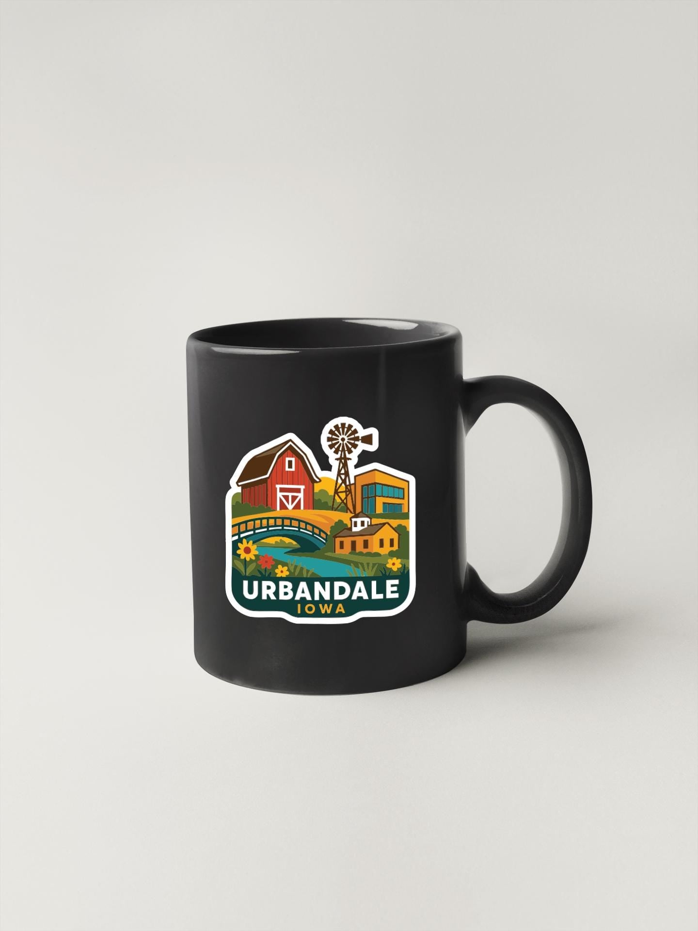 A black coffee mug with a colorful illustration of a rural town and a windmill on it, along with the text "URBANDALE" printed on it.