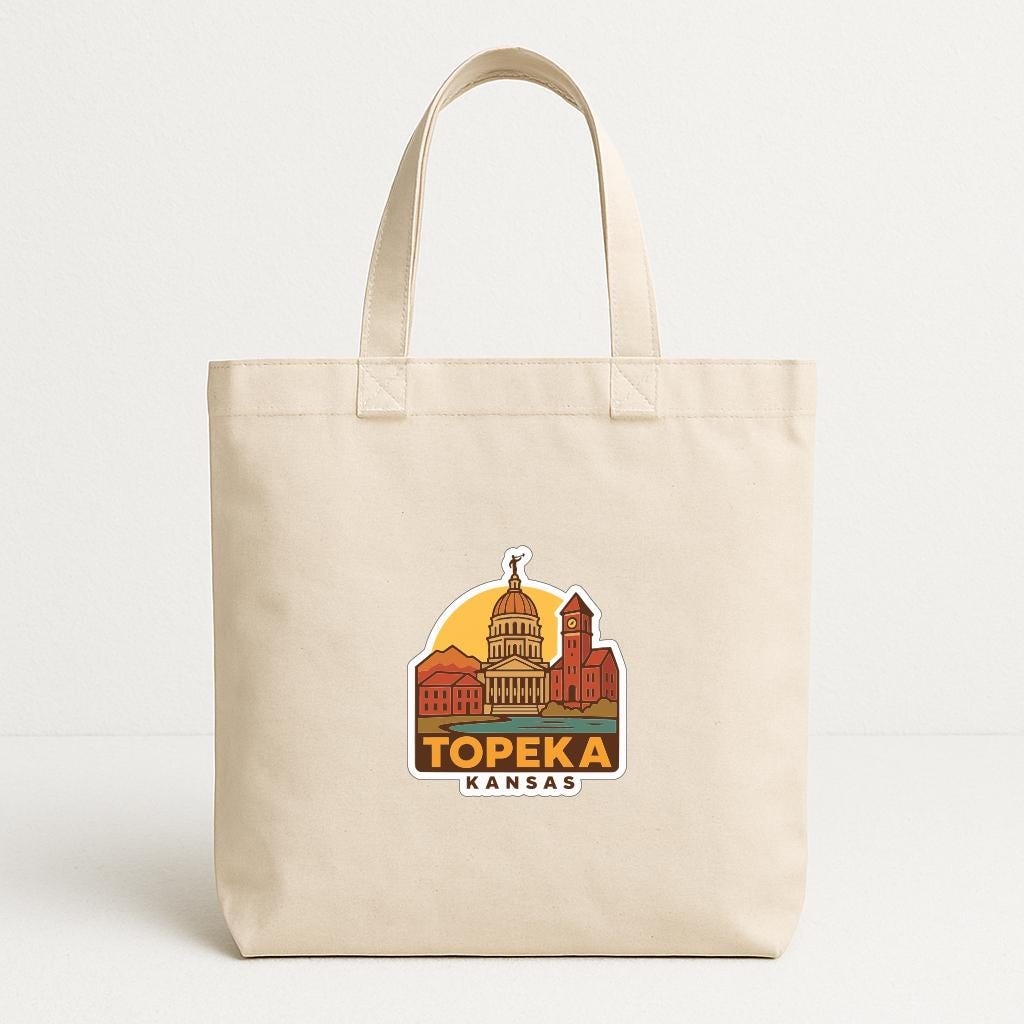 A beige tote bag with a printed design of the Topeka, Kansas skyline.