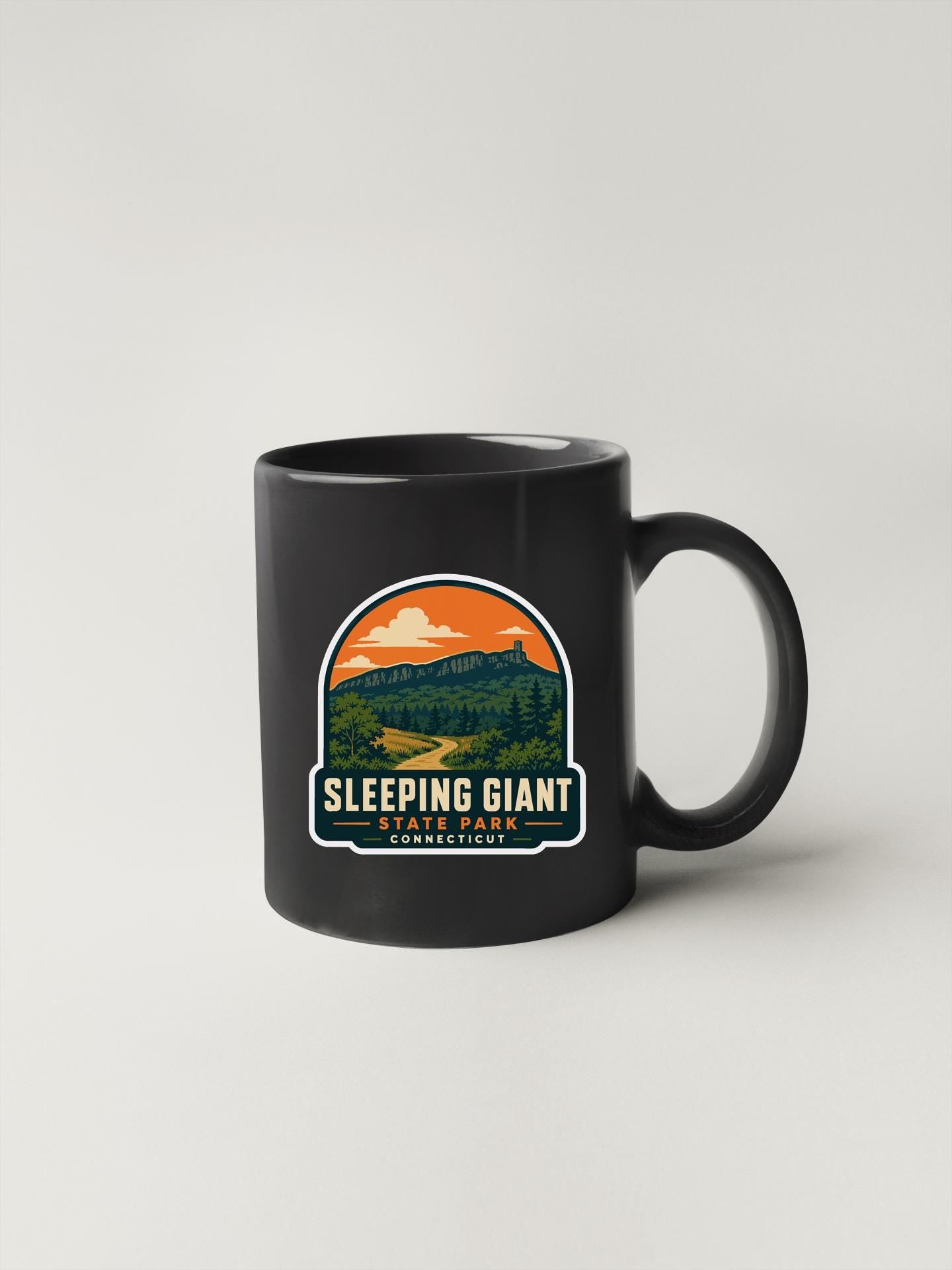 A black coffee mug with a graphic design depicting a scenic mountain landscape and the text "SLEEPING GIANT STATE PARK CONNECTICUT".