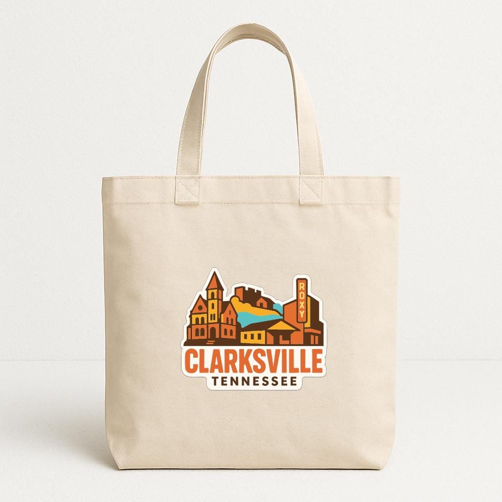 A beige tote bag with a graphic design depicting a cityscape and the text "CLARKSVILLE TENNESSEE" printed on it.