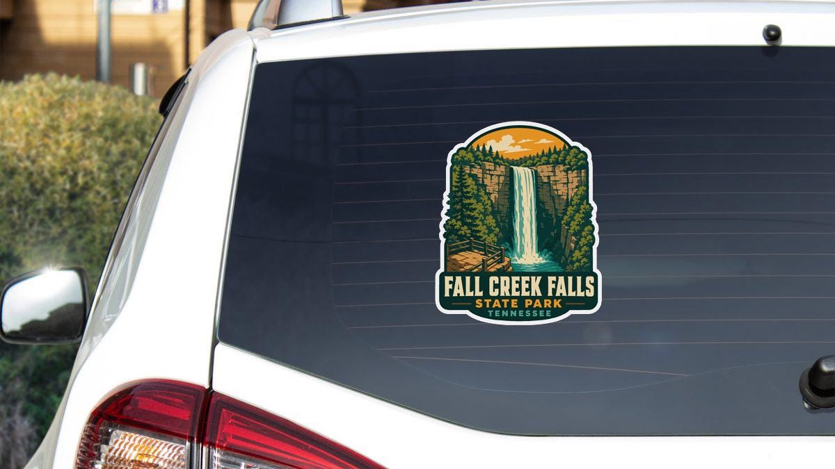 A sticker on the rear window of a white vehicle, depicting a scenic waterfall surrounded by trees and mountains.