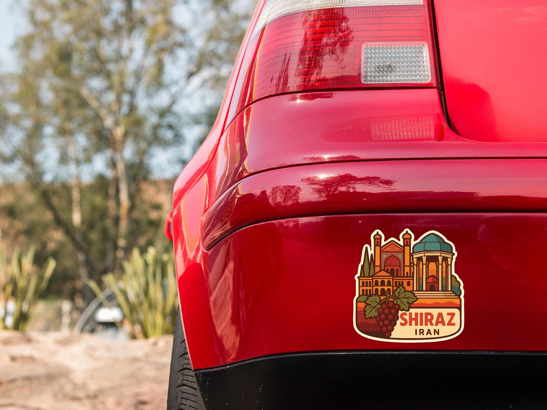 the rear end of a red car with a sticker on the trunk that features an illustration of a building and the text "SHIRAZ IRAN".