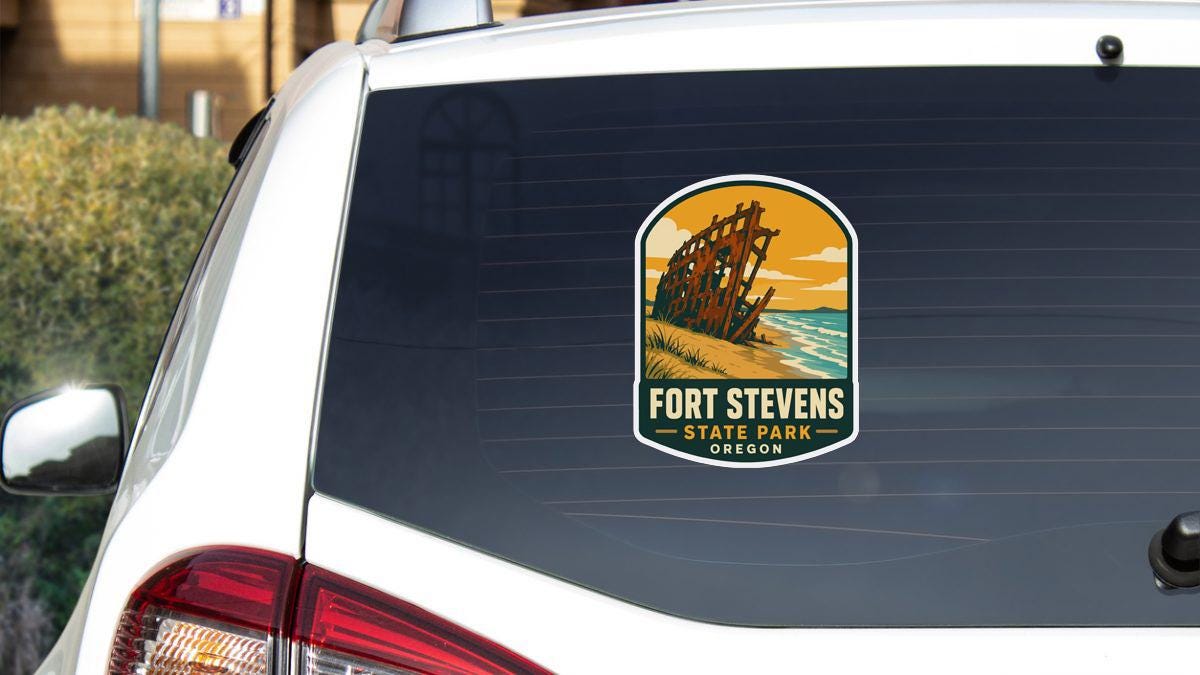 A sticker on the rear window of a white car, depicting a scenic view of Fort Stevens State Park in Oregon.