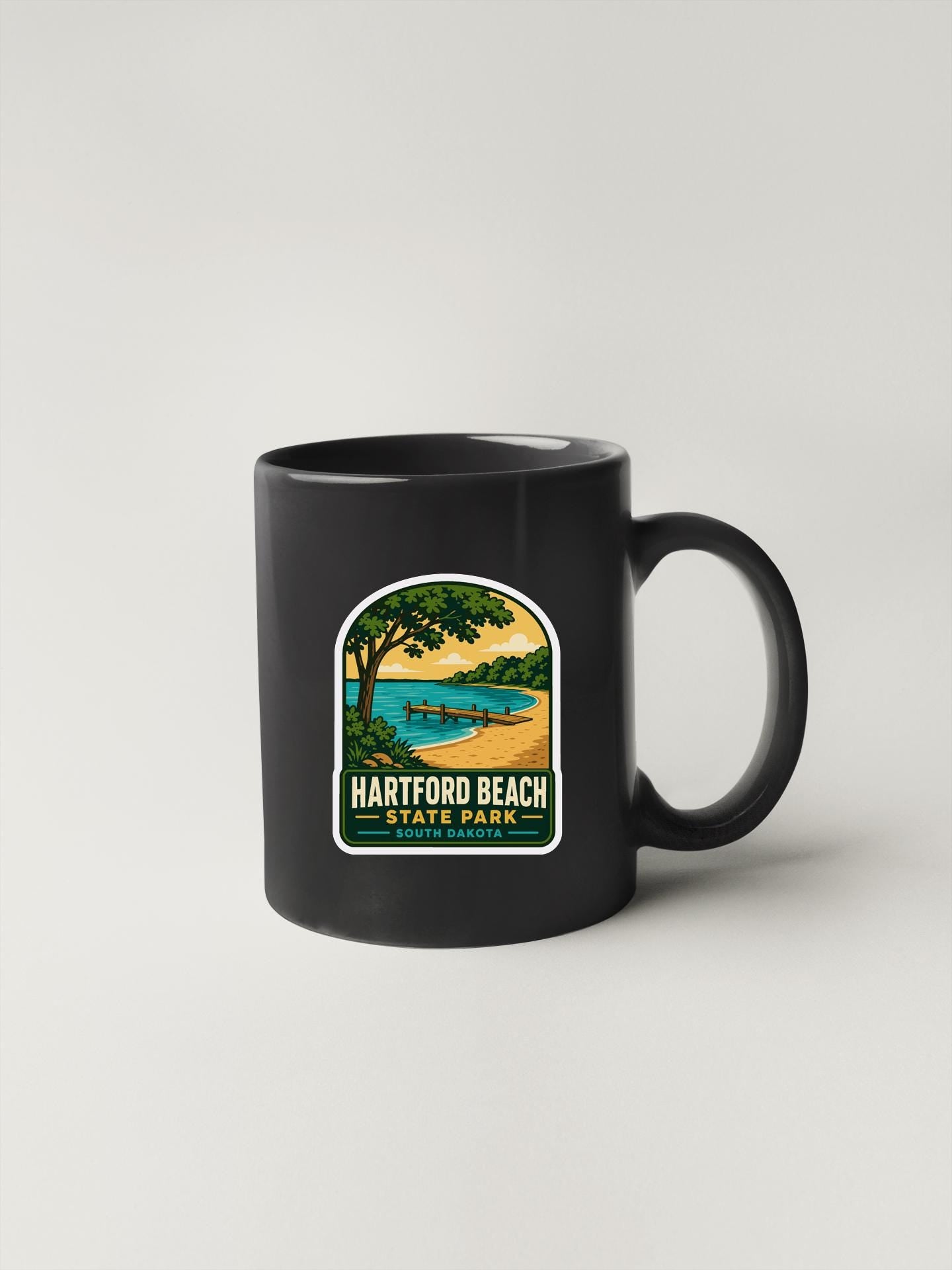 A black coffee mug with a graphic design depicting a scenic beach landscape, including a tree, a body of water, and a sunset.