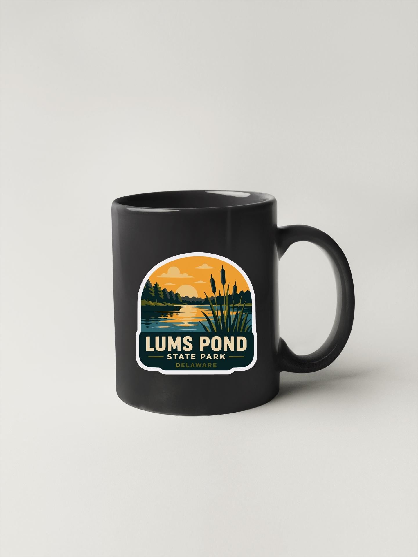 A black coffee mug with a graphic design depicting a lake and a sunset, along with the text "LUMPS POND STATE PARK".