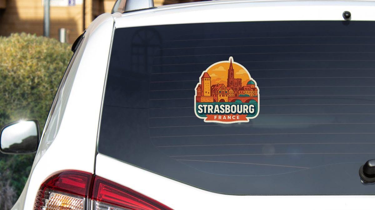 A sticker on the rear window of a white car, depicting the city of Strasbourg, France.