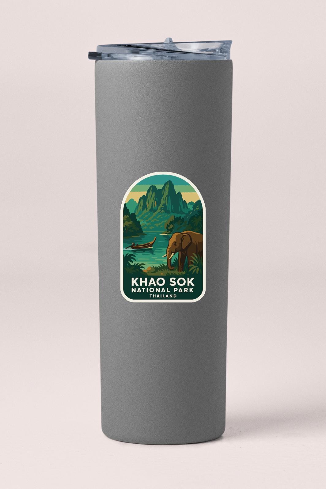 A gray cylindrical container with a label that features an illustration of a landscape with mountains, a river, and an elephant.