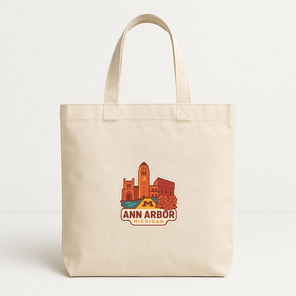 A beige tote bag with a printed design of a city skyline and the text "ANN ARBOR MICHIGAN" printed on it.