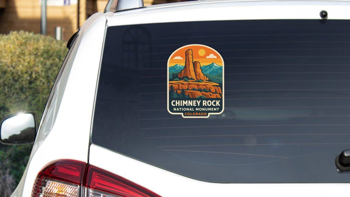 A sticker on the rear window of a white car, depicting a scenic mountain landscape with a prominent rock formation.
