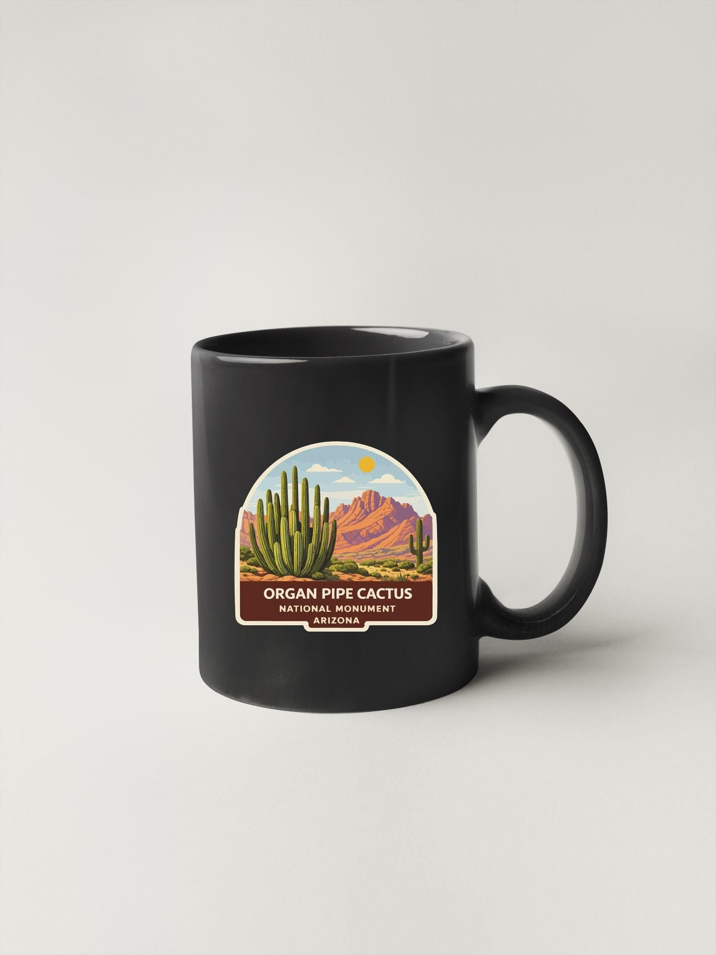 A black coffee mug with a label that features an illustration of a cactus and mountains, along with the text "ORGAN PIPE CACTUS NATIONAL MUNICIPALITY ARIZONA".