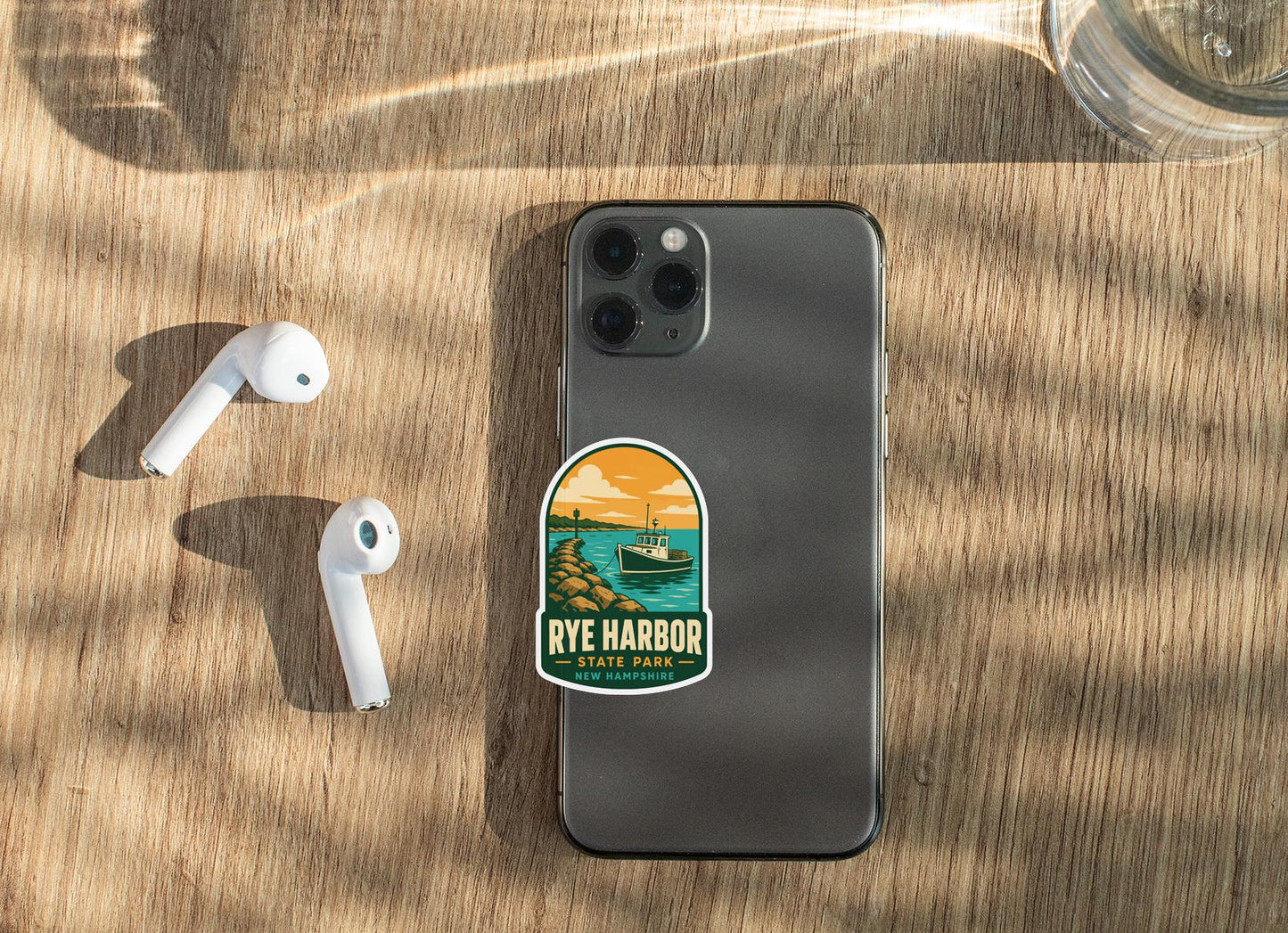 a smartphone with a sticker on it, placed on a wooden surface alongside a pair of white earbuds.